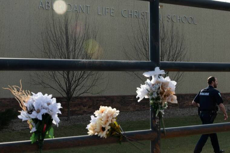 REUTERS/CULLEN GRANZEN
A police officer passes flowers left in memory of victims a day after a shooting at Abundant Life Christian School, in Madison, Wis., on Tuesday.